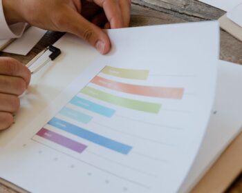 Close-up of hands reviewing business report with colorful charts and graphs on a wooden desk.